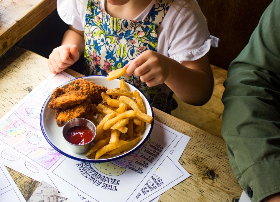 A child sat at a table eating from a plate of breaded chicken and chips