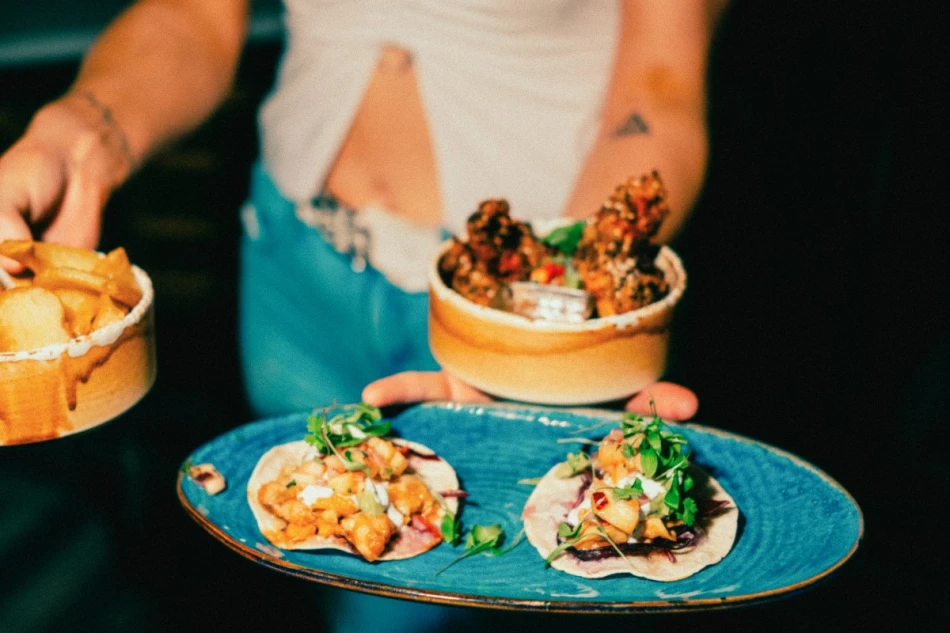 A woman carrying plates of food including two tacos arranged on a blue plate