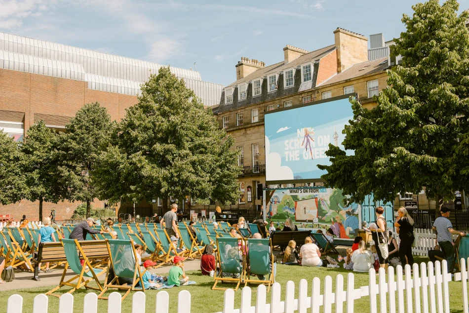 People sat on a temporary grassed area watching a movie on a big cinema screen