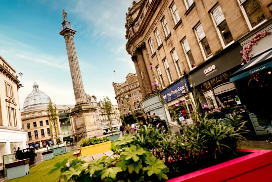 Newcastle's Grainger Street, looking towards Grey's Monument with green space and plants in the foreground.