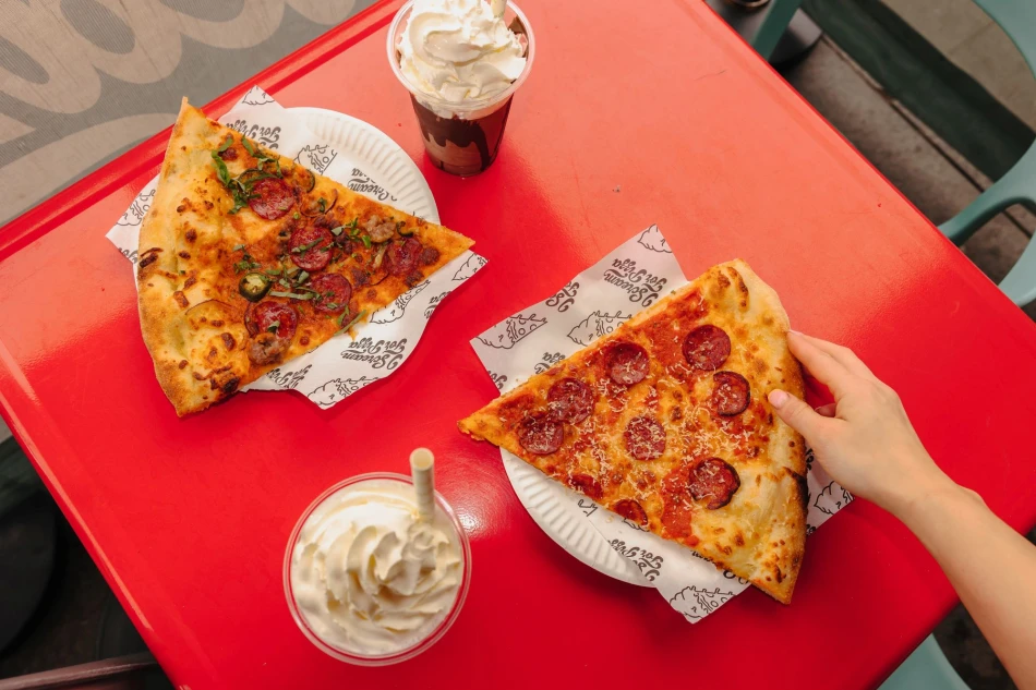 Two slices of pizza on plates on top of a bright red table